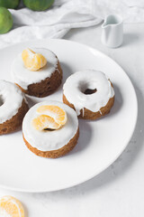 Mini bundt cakes covered in a white glaze on a white countertop, small vanilla bundt cake with a white glaze and tangerine segment on a white background