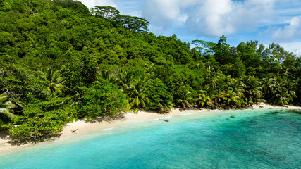 Sandy beach with lush green vegetation touches turquoise waters. Seychelles, Mahe. Butzel Beach.