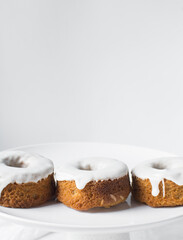 Mini bundt cakes covered in a white glaze on a white countertop, small vanilla bundt cake with a white glaze and tangerine segment on a white background