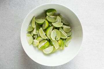 Overhead view of chopped limes on a white background, top view of quartered limes being prepared