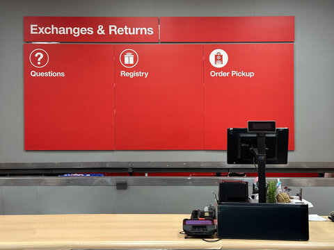 Customer service counter with a red signage board above it for exchanges, returns, questions, registry, and order pickup. The counter has a point-of-sale monitor.