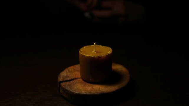 Woman hand lights a match the bees wax candle on wooden candlestick for mood, relaxation, meditation dark black background. Person lighting the decoration handmade one candle flame. Video with sound