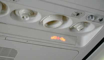 The seat belt light on the plane is on. Warning passengers to fasten their seat belts during the flight. Illuminated seatbelt sign in an airplane. Airplane safety sign. 