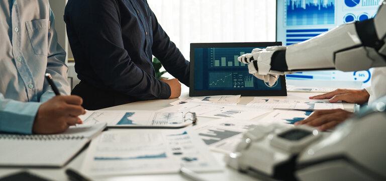 A business team engages in a meeting featuring artificial intelligence technology. Interactive charts and graphs are displayed, showcasing data analysis in a modern office setting.Noogenesis