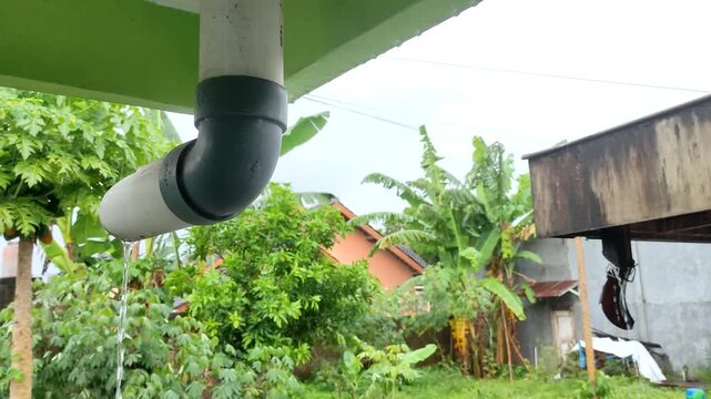 Rainwater dripping from roof drainage pipe in tropical residential area, background rain sounds relaxation meditation