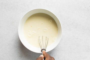 overhead view of custard being mixed in a white bowl, process of making cooked custard