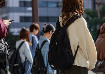 Person engrossed in his phone as diverse group of college students with backpacks wait traffic...