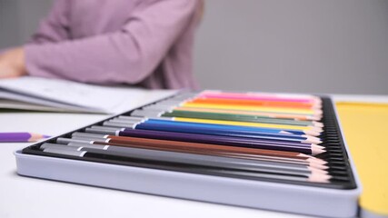 Child's hands choosing a blue colored pencil from a metal tin on a desk, preparing to draw and color as part of creative play, learning and artistic exploration - Powered by Adobe