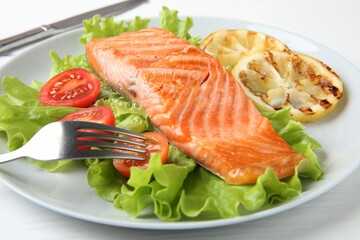 Piece of tasty grilled salmon, lemon slices and salad on white table, closeup