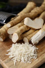 Grated horseradish, grater and fresh roots on wooden table, closeup