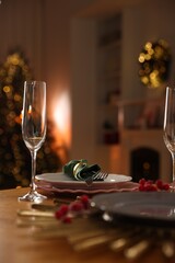 Christmas table setting with plates and glasses in festive decorated room, closeup