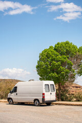 White camper van parked on a dirt road next to a green tree under a blue sky in Andalusia, Spain