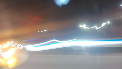 Brightly colored lines of light extend in rapid motion across the dark asphalt, creating a dramatic...