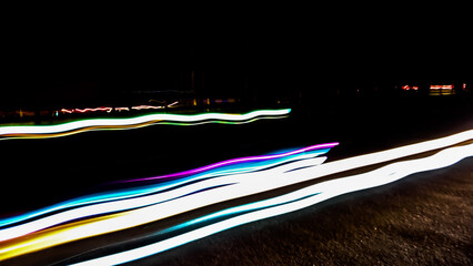 Brightly colored lines of light extend in rapid motion across the dark asphalt, creating a dramatic...