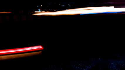 Brightly colored lines of light extend in rapid motion across the dark asphalt, creating a dramatic...