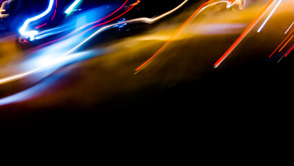 Brightly colored lines of light extend in rapid motion across the dark asphalt, creating a dramatic...