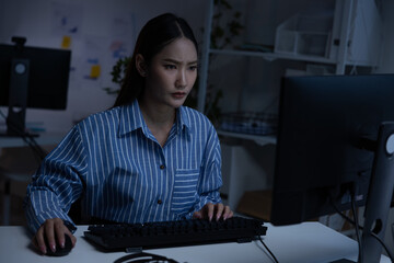 Asian focused night work woman typing on computer in office late evening determined expression serious mood