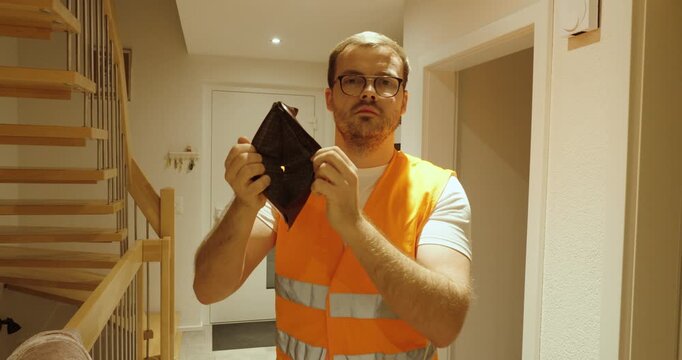 A worker in an orange safety vest holds up an empty wallet, symbolizing low pay, financial struggle, and lack of savings or pension.