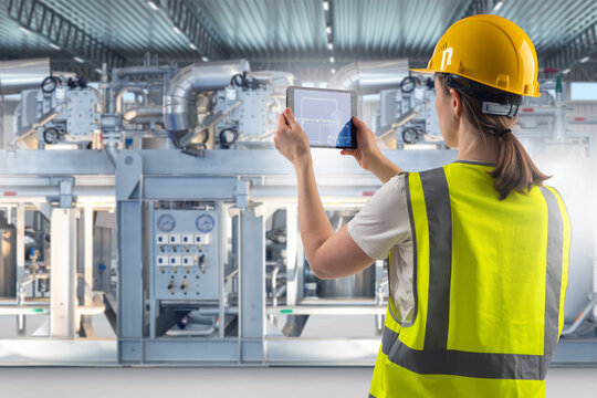 Industrial equipment inspector reviews machinery performance using a digital tablet, checking system schematics and verifying operational parameters in a modern production facility.