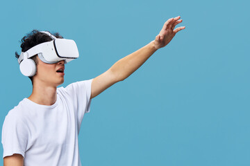 young man wearing virtual reality headset reaching out, immersive technology experience, casual white t-shirt, blue background, digital interaction