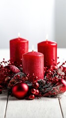 Three red candles are lit on a table with red berries and balls