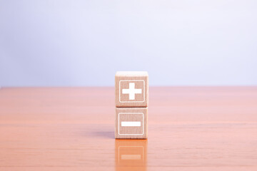 Wooden blocks with plus and minus symbols representing comparison, decision-making, pros and cons,...