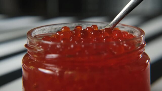 Close-up view of a spoon lifting glossy red caviar from a glass jar, sparkling roe and rich texture, premium seafood delicacy and celebration cuisine concept