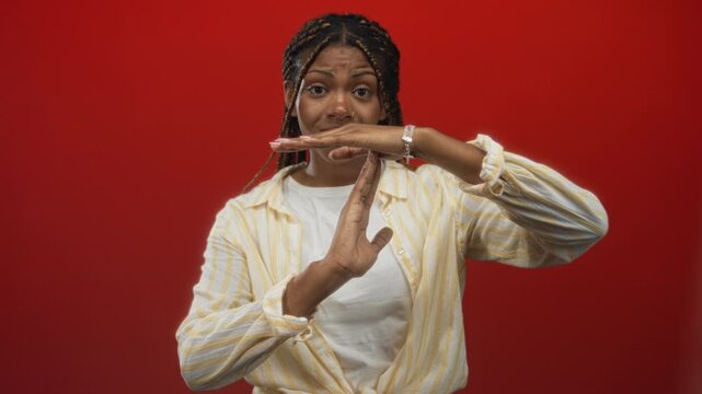 Woman showing timeout sign with hands in red studio, braided hair and bracelet visible; boundary setting assertive.