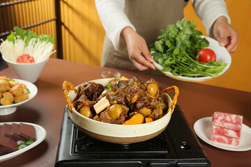 Chef Preparing Hot Pot Lamb Dish with Fresh Vegetables and Herbs in Traditional Restaurant Kitchen