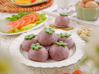 Purple steamed buns with green flower garnish breakfast spread with vegetables and eggs on white table