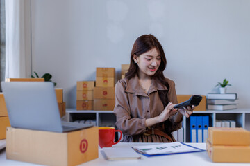 SME supply chain concept, procurement, Asian female entrepreneur taking notes while working on laptop, customer is managing orders in small business store.

