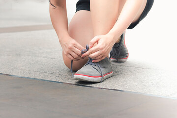 Sport sneakers footwear young woman knelt down do up shoelaces. Ready running shoes in sport exercise jogging person. Close up hands tie up runner shoelaces in fitness gym healthy person lifestyle.
