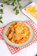 Golden Crispy Pork in Sweet and Sour Sauce with Orange Garnish on Decorative Plate