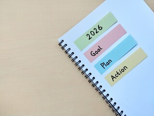 New year 2026 resolution concept. Goal, plan and action written on colorful sticky note on notebook with wooden table background. Copy space. Flat lay 