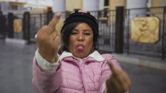 Woman in pink jacket and helmet gestures provocatively in outdoor city setting with focus on self-expression and attitude.