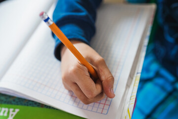 Child hand writing homework on checkered notebook