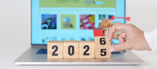 2025 end year to Happy New Year 2026 block with shopping trolley cart on table. E commerce, online shopping, finance, consumer economy and celebration concepts