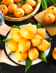 Fresh Loquat Fruits from Yunnan Mountains China in Traditional Bamboo Basket with Green Leaves on Wooden Table