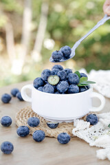 Fresh Organic Blueberries in White Cup with Spoon on Rustic Wooden Table Outdoors