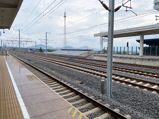 Modern High speed Train Station Platform with Multiple Railway Tracks and Overhead Power Lines Under a Cloudy Sky, Showcasing Infrastructure