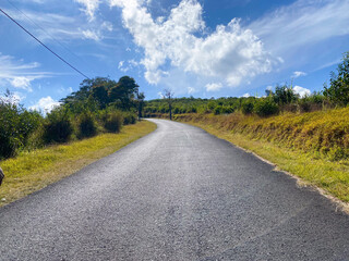 Paved Road Winding Through Lush Green Hills Under a Bright Blue Sky with Scattered White Clouds