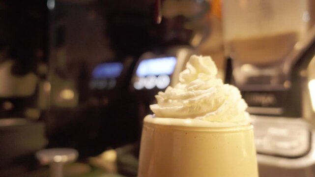Close-up of rich chocolate syrup being drizzled over a mountain of fresh whipped cream on a cold drink