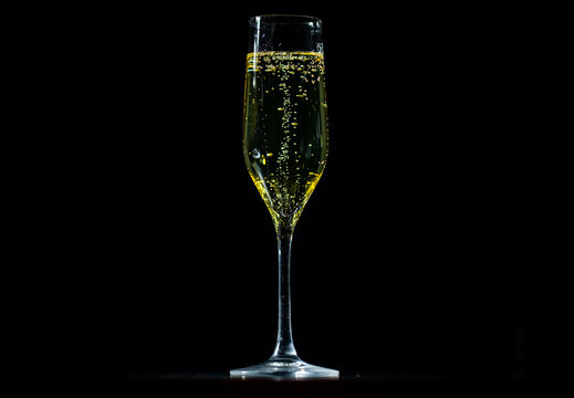 Champagne sparkling in a crystal glass. Pouring bubbly champagne with festive bubbles. Close-up of sparkling wine splash in elegant wineglass. - Powered by Adobe