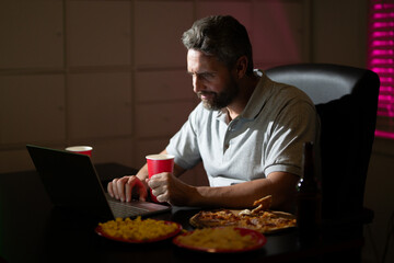 Business man eat pizza during a late night at office. An overworked man works on his laptop while having dinner in the workplace. A manager eat takeaway meal while finishing office work at night.