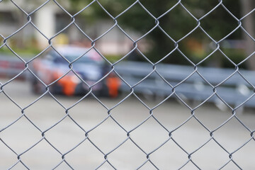 Selective focus on metal chain link fence creating an abstract wire mesh pattern. blurred race car in background evokes feeling of security and separation