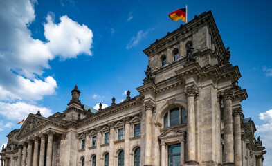 German flag over Reichstag. Corner view of Reichstag Berlin. Historic government architecture. German landmark with flag. Historic Reichstag architecture in Berlin. Political symbol of Germany.