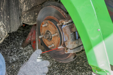 Focused mechanic performing car repair and brake maintenance. hand in glove spraying lubricant on rusty rotor and caliper for vehicle service and careful work