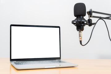 Laptop with blank white screen and professional studio microphone setup for podcast recording workspace