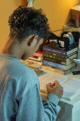 A boy is checking gold price charts on a smartphone while holding a gold bar package at a desk with books and a clock in the background, shot in portrait view from behind