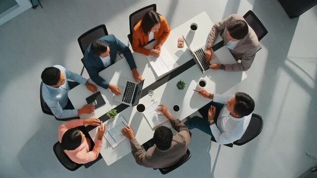 Cinematic 4K top-view of six colleagues brainstorming with documents and laptops, ultra-clean white workspace, shadowless lighting, calm corporate atmosphere